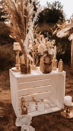 a white table topped with vases filled with flowers and candles on top of a dirt ground