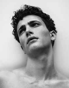 a man with curly hair and no shirt on is looking up at the sky in front of a white wall