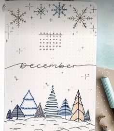 a notebook with christmas trees and snowflakes on it, next to a pen