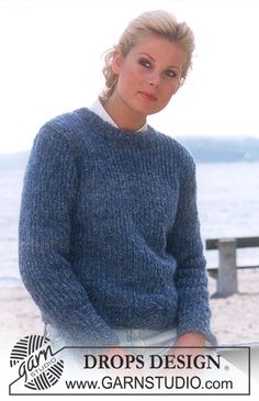 a woman standing on the beach wearing a blue sweater