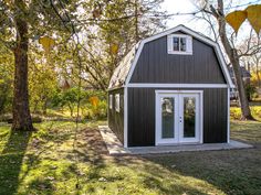 a black and white barn style house in the middle of some grass with trees around it