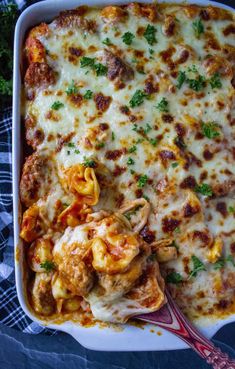 a casserole dish with meat, cheese and vegetables in it on a blue table cloth