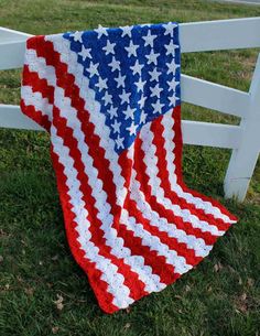 an american flag quilt is draped over a white fence in the grass on a sunny day