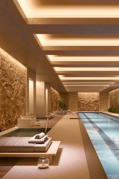 an indoor swimming pool with lounge chairs and lights on the ceiling, along with stone walls