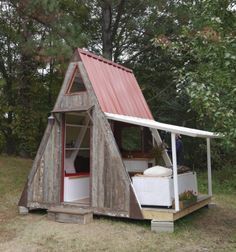 a small wooden structure with a red roof in the middle of some grass and trees