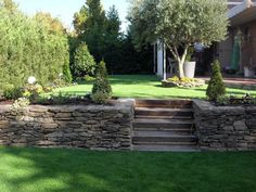 a stone wall with steps leading up to it in the grass next to a house