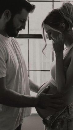 a man and woman standing next to each other in front of a window while talking on the phone