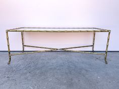 a gold metal and glass coffee table with two legs on the top, in front of a white wall