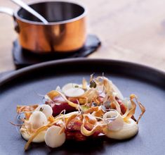 a black plate topped with food on top of a wooden table next to a pot