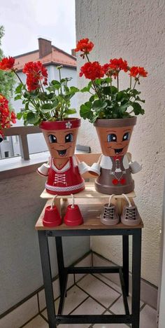 two potted plants sitting on top of a wooden table with red flowers in them