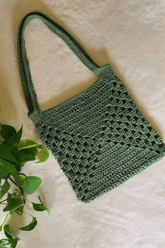 a green crocheted bag sitting on top of a white blanket next to a plant