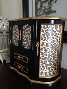 an ornate black and gold cabinet with leopard print on the doors, in front of a mirror