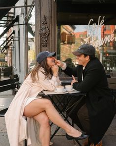 a man and woman sitting at a table talking to each other in front of a coffee shop