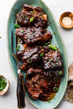 some meat on a blue plate with green onions and seasoning next to other dishes