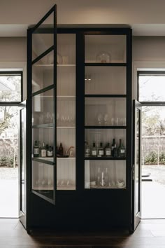 an empty glass cabinet in the middle of a room with doors open to let in light