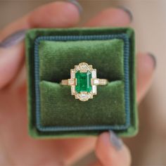 a person holding an emerald and diamond ring in a velvet box with green velvet lining