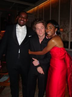 two men and a woman in formal wear posing for the camera