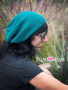 a woman wearing a green knitted hat looking at her cell phone in front of some flowers