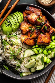 a bowl filled with rice, cucumber and chicken next to chopsticks