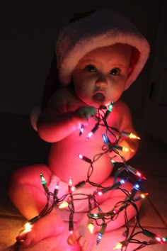 a baby is sitting on the floor with christmas lights