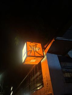 an orange sign hanging from the side of a tall building at night with lights shining on it