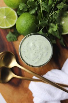 a wooden table topped with limes and two gold spoons next to a jar of ranch dressing