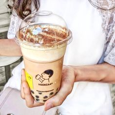 a woman holding up a cup of coffee with whipped cream on top and chocolate sprinkles in it