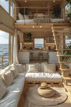 a living room filled with furniture and lots of windows next to the ocean on top of a wooden floor