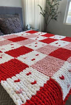 a red and white crocheted blanket sitting on top of a bed next to a window