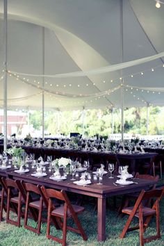 an outdoor tent with tables and chairs set up for a formal dinner or party in the grass