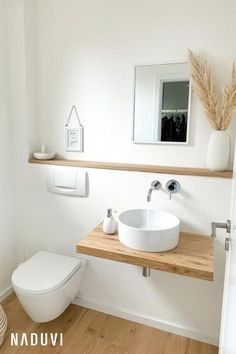 a white toilet sitting next to a bathroom sink under a mirror on top of a wooden counter