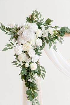 white flowers and greenery decorate the top of a wedding arch