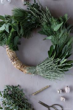 the wreath is surrounded by greenery, scissors and other crafting supplies on a table