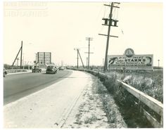 an old black and white photo of cars driving down the road in front of a sign