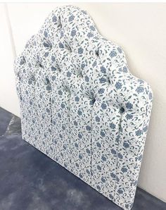 an upholstered headboard with blue and white flowers on the top, against a wall