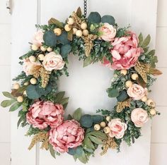 a wreath with pink flowers and greenery hanging on a white front door or wall