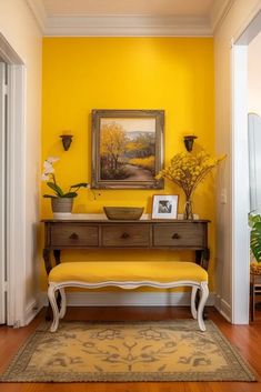 A beautiful yellow entryways with a yellow accent wall, a wooden framed yellow landscape art print, dark wooden vintage table with three drawers and wooden knobs, vase, potted plant, storage tray and a picture frame. Next to the entryway table is a vintage wooden bench painted in white and with upholstered yellow fabric. A yellow patterned rug to complete the mood. Yellow Mudroom, Yellow Entryway, Yellow Front Doors, Entryway Door, Door Table, Central Idea, Small Entryways, Yellow Decor, Yellow Interior