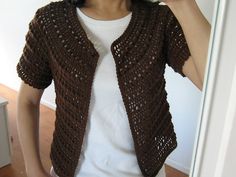 a woman taking a selfie in front of a mirror wearing a brown crocheted cardigan