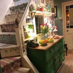 a kitchen with green cabinets and stairs leading up to the upper floor, decorated with flowers