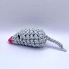 a small crocheted mouse is shown on a white surface with a pink nose