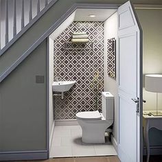 an open door leading to a bathroom with a toilet and sink under the stair case