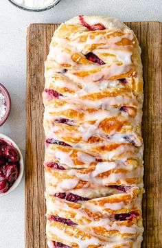 a loaf of fruit bread with icing on a cutting board next to some cranberries