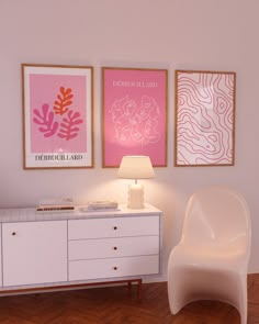 a white chair sitting next to a table with a lamp on it in front of two pictures