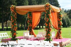 an outdoor wedding setup with white chairs and orange drapes