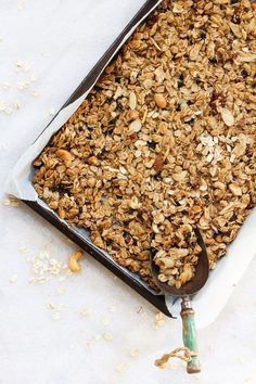 a pan filled with granola sitting on top of a white table next to a spoon