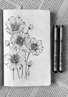 two pens are sitting on top of an open book with flowers drawn on the pages