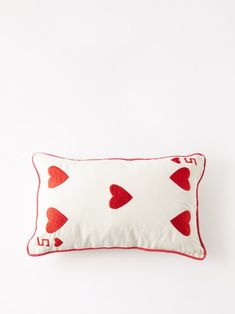 a red and white pillow with hearts embroidered on it's side, against a white background