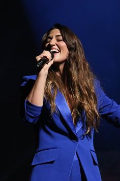 a woman in a blue suit singing into a microphone with her hands out to the side