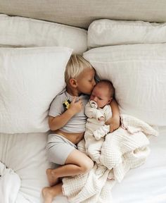 two babies are laying on top of each other in the middle of a white bed