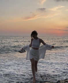 a woman standing on top of a sandy beach next to the ocean at sunset or dawn